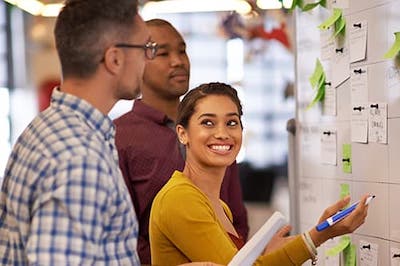 people standing at a whiteboard with post-it notes and dry erase markers