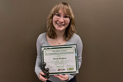 Olivia Basiliere smiling while holding a Daisy award certificate and trophy