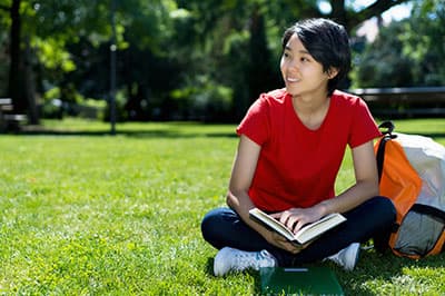 Girl sitting in the grass with backpack and book