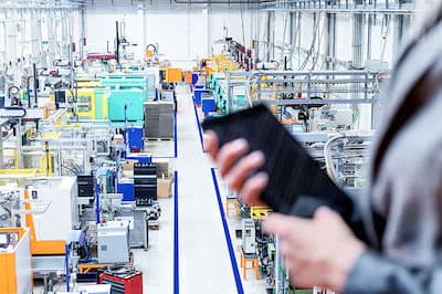 person overlooking manufacturing plant with tablet in-hand