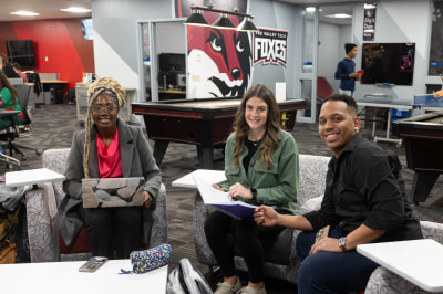 FVTC students sitting in chairs in the Student Life room with FVTC foxes logo and image on the wall behind them