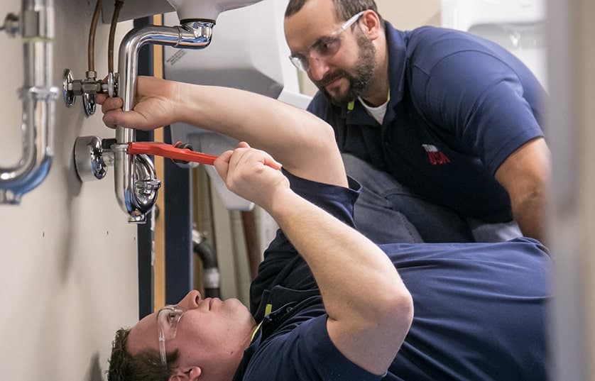 student learning plumbing lying under a sink