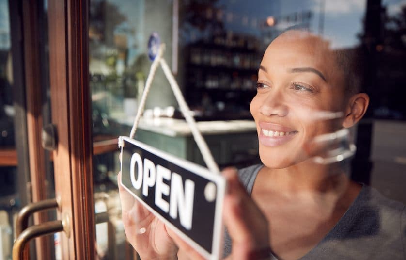 woman turning open sign on retail store door
