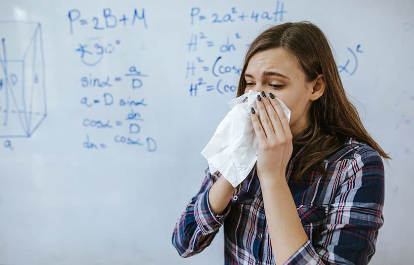 person sneezing into kleenex standing in front of whiteboard