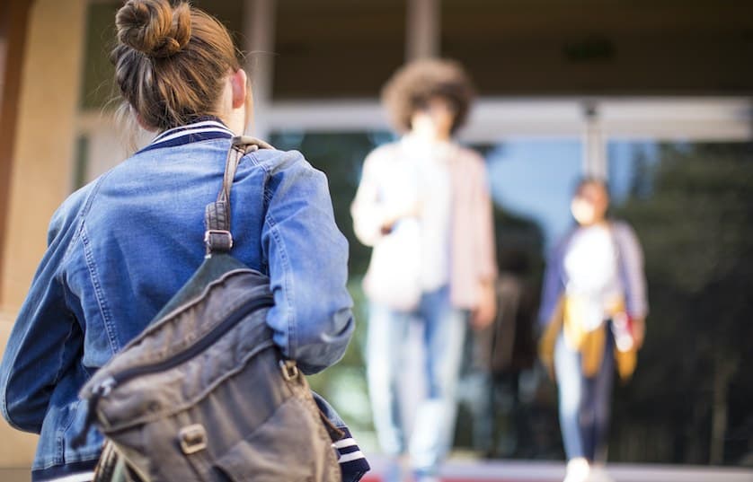 person with jean jacket and backpack walking toward entrance of building