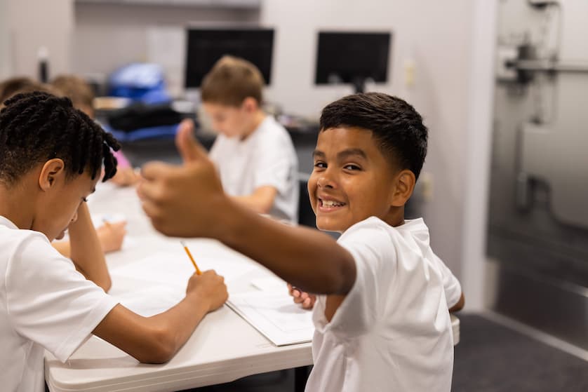 Summer camp participant smiling at camera giving a thumbs up