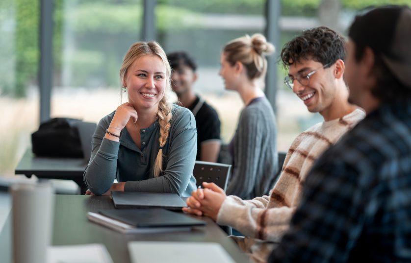Student smiling at a table with several other students sitting