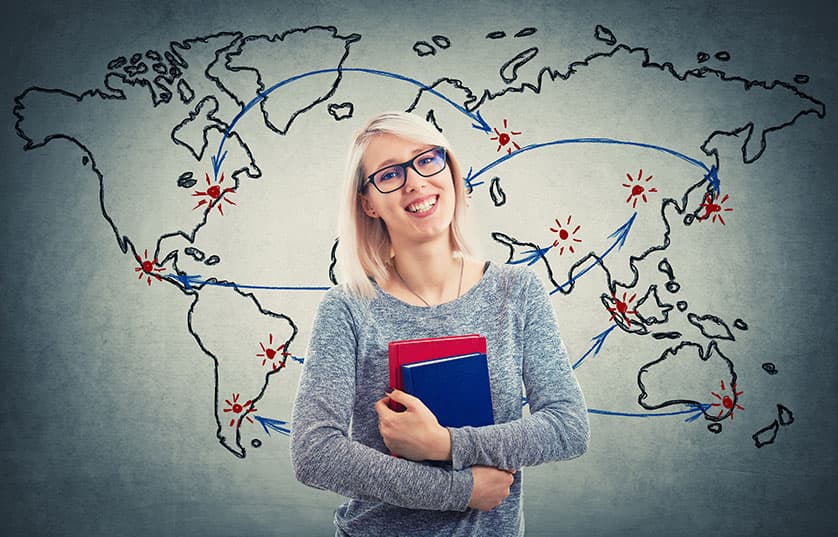 student holding books standing in from of map of the world