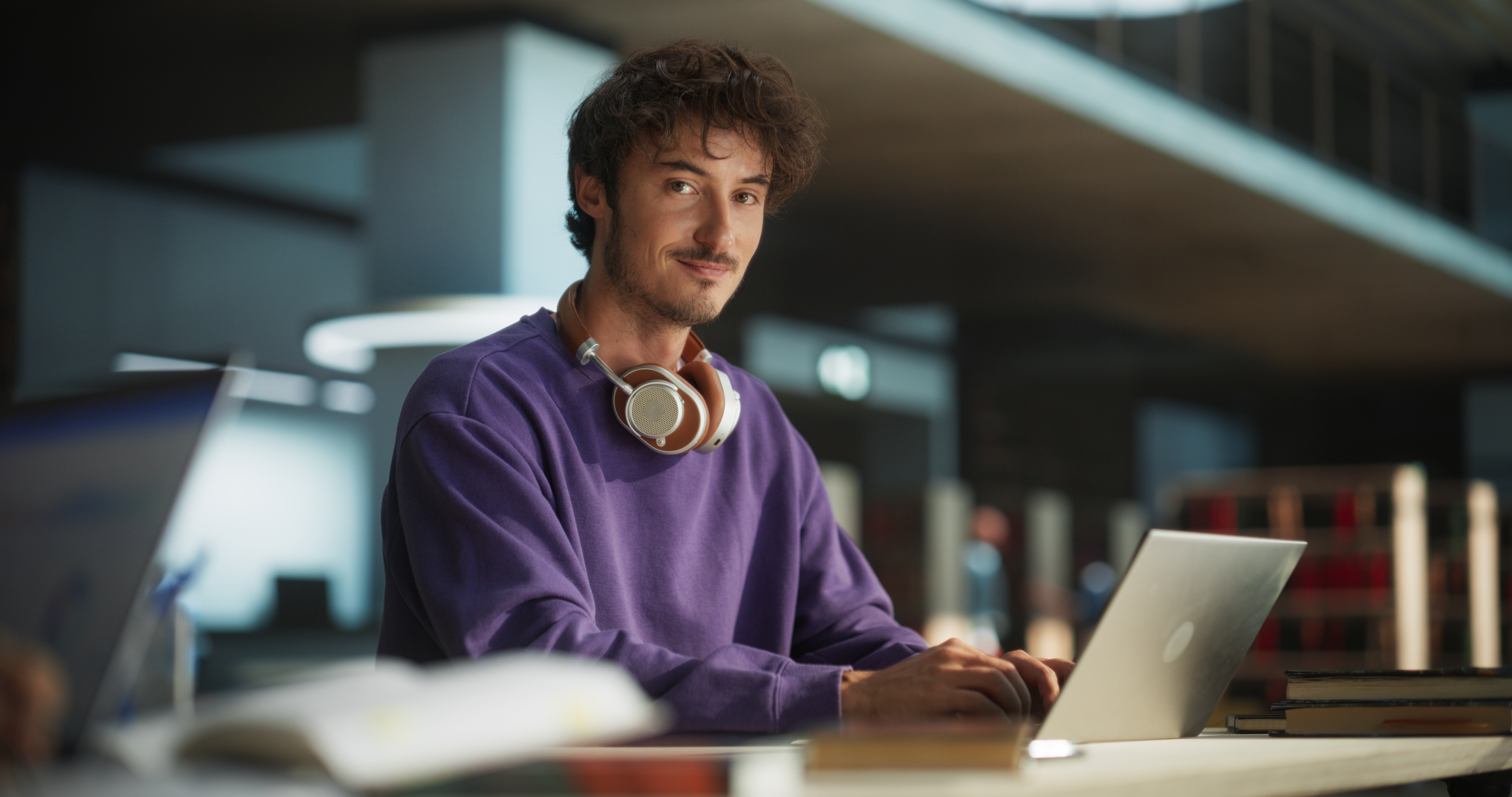 student smiling at camera sitting at desk typing on computer