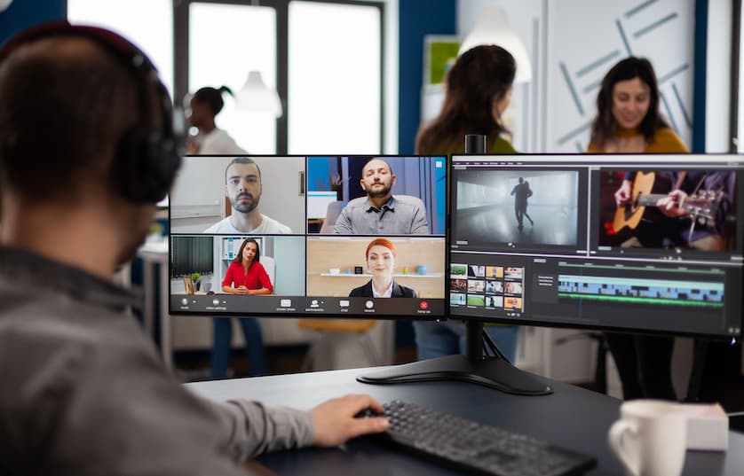 person with headphones sitting in front of two monitors on virtual meeting