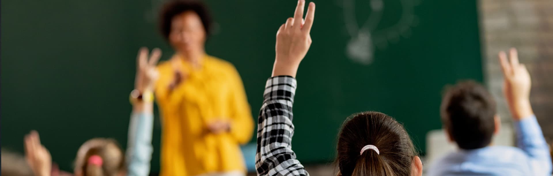 teacher with students raising their hands in classroom