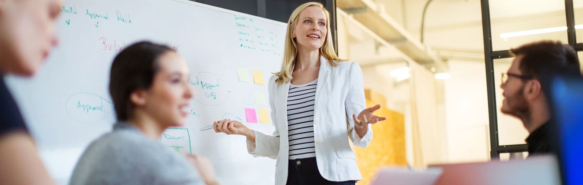 woman standing at whiteboard leading an office meeting