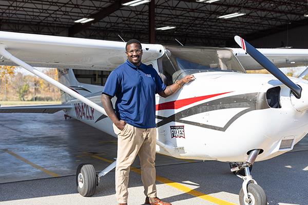 Male student standing next to small airplane outside airplane hanger