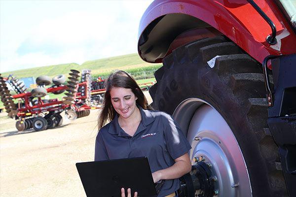 woman standing with laptop computer next to farm equipment