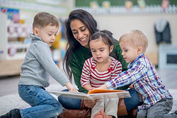 teacher reading book to three small children