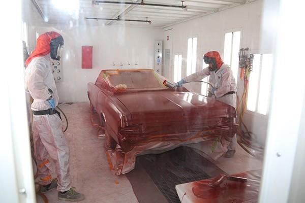 two people painting car in refinishing shop