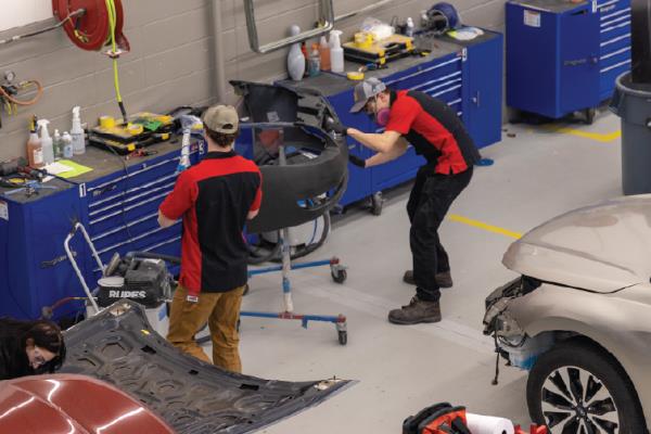 two people painting car in refinishing shop