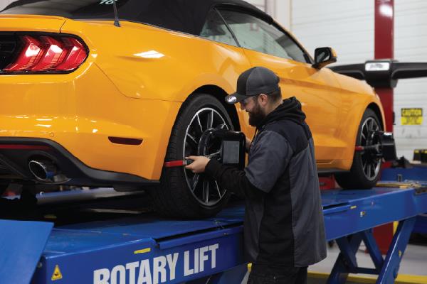 smiling man wearing goggles holding device next to car in automotive shop