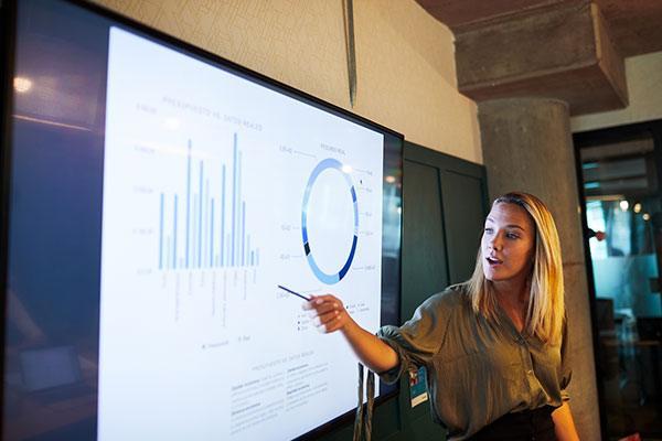 woman standing in front of a presentation pointing to a bar chart