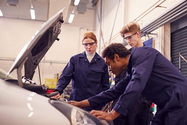 Male teacher with students looking at a car engine