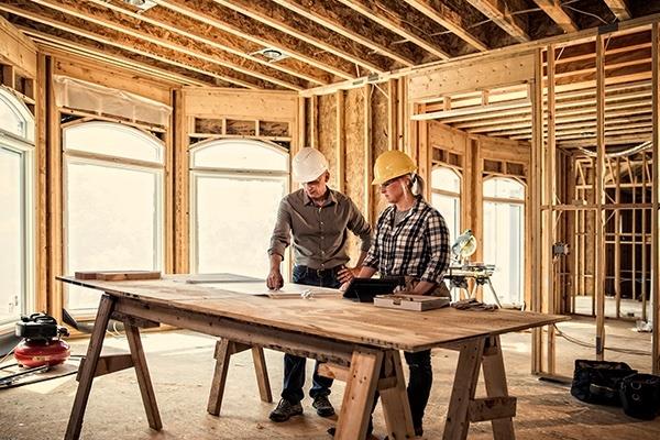 two construction workers in hardhats looking at plans on workbench at construction site