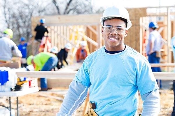 construction worker standing at construction site with several construction workers in background all in hardhats