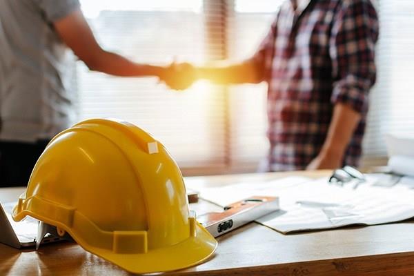 hardhat and level on desk with two construction workers shaking hands in background