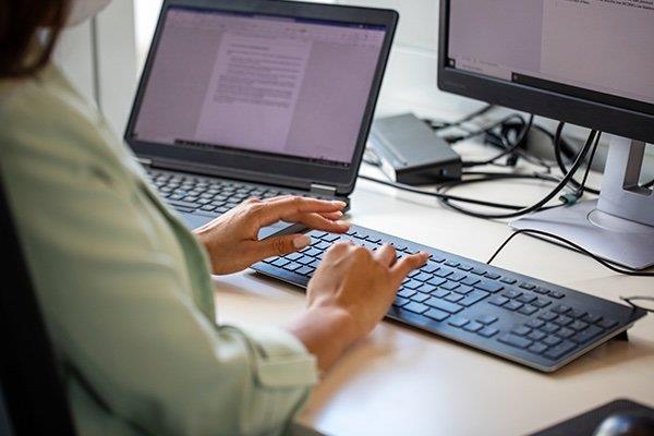 person typing on keyboard in front of monitor and laptop