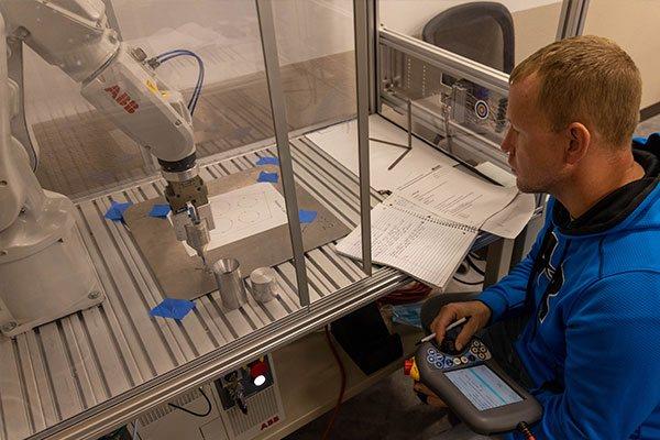 person working with control panel watching a mechanical machine arm