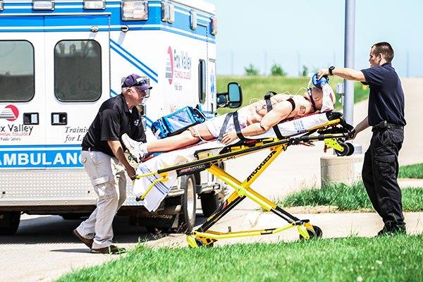 two EMTs rolling gurney with patient simulated dummy toward ambulance