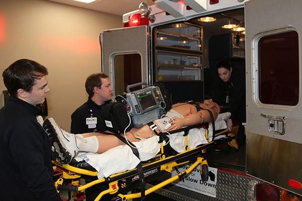 EMT students rolling gurney with dummy into back of ambulance