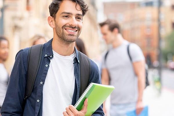 smiling man with notebook walking with buildings and other people in background