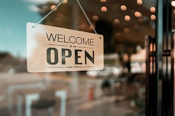 wooden sign hanging in window that reads welcome we are open please come in