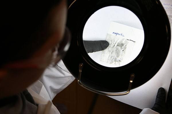 person in lab looking at evidence under microscope