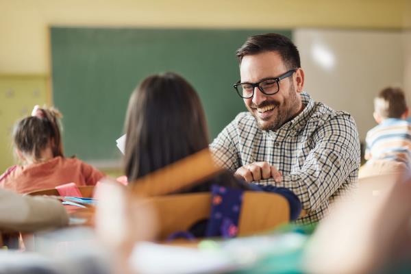 teacher in front of chalkboard with students in foreground raising their hands