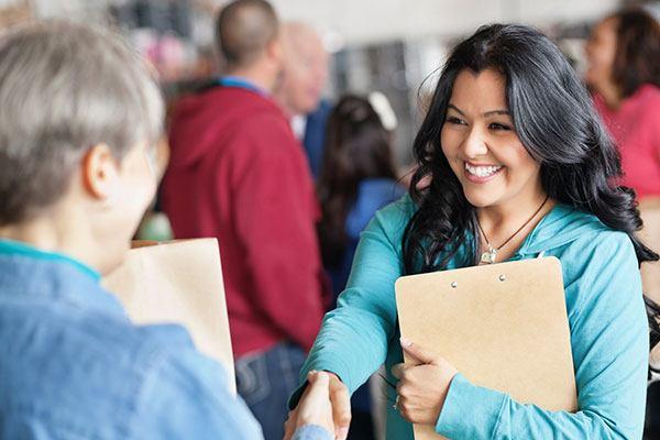 smiling woman with clipboard shaking hands with other people in background