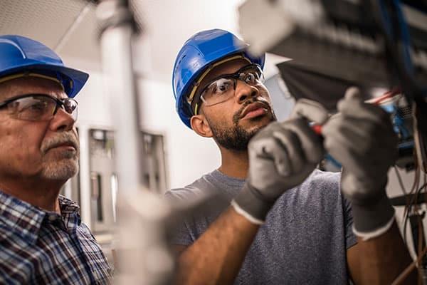 two men in hardhats and safety glasses working on machine