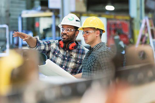 two men in shop wearing hardhats with building plans