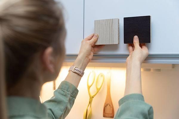 person comparing cabinet sample blocks against white cabinet door