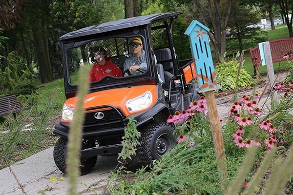 two people riding in side-by-side UTV on sidewalk near gardens