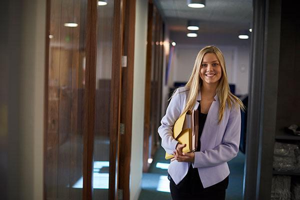 woman in blazer walking down office hallway with files under her arm