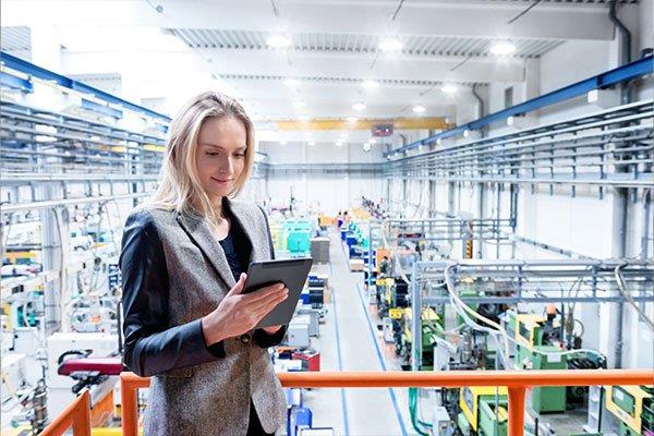 woman holding digital tablet standing on platform overlooking manufacturing plant