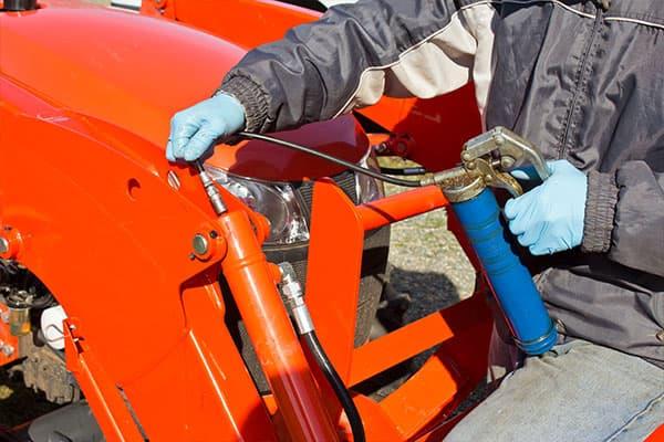 person with gloves adding lubricant to tractor bucket mechanism