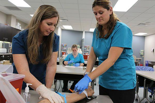 student and instructor in a phlebotomy lab drawing blood