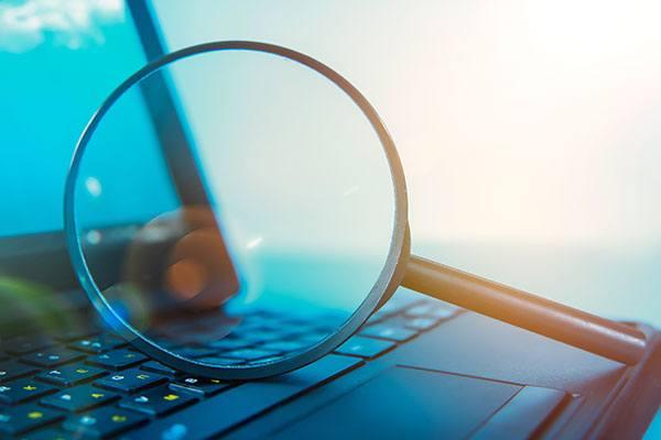 large magnifying glass laying sideways on open laptop keyboard keys