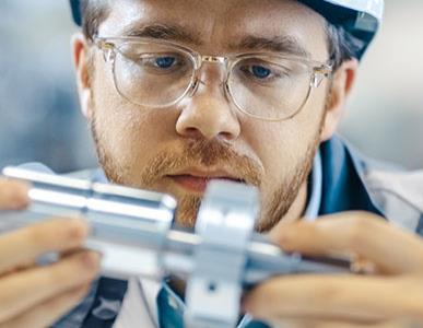 man in glasses holding a metal machine part