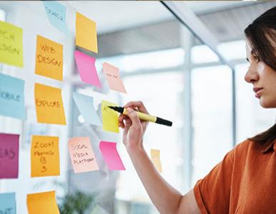 woman writing on wall of sticky notes