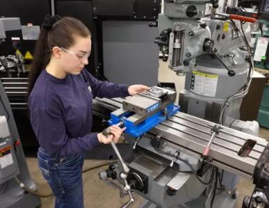 female machinist with safety goggles working on a precision metal machine