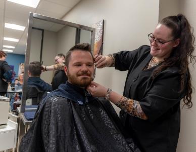 student trimming a man's beard in the trilogy salon