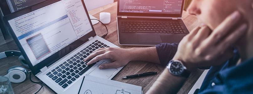 man working on software development coding on two laptops and monitor